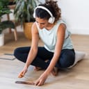 young woman getting ready for meditation with headphones on, lighting incense in front of her