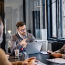 male team leader with laptop in front of him guiding discussion on project with his team in a meeting room