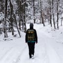 Back view of a young girl strolling through a dense forest during winter, with snow all around her.