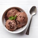 Bowlful of chocolate ice cream with some chocolate and a spoon beside