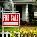 close-up of a "For Sale" sign posted in front of a family home