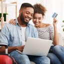 A couple sitting on a couch in their living room booking a trip on a laptop