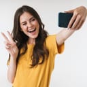 Image of beautiful brunette woman laughing and showing peace sign while taking selfie photo