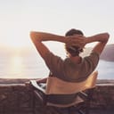 Man at the seaside sitting in chair enjoying the view of sunset