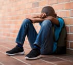 A sad elementary age schoolboy sitting on the floor with hands crossed on knees