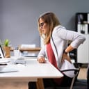 Woman holding her lower back in pain while sitting in an office