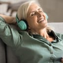 close-up of an elderly woman enjoying music on her cellphone with wireless headphones, sitting on the sofa at home
