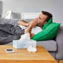 A man sick with cold lying on the sofa blowing his nose into a tissue