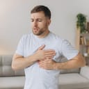A young man standing in his home, clutching his chest in distress, experiencing intense pain.