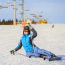a woman in a blue ski suit trying to get up after falling on a mountain slope