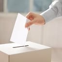 Closeup of hand inserting envelope in ballot box