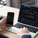 close-up of a businessman viewing stock market data on smartphone and laptop