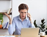 A female visibly irritated talking on the phone and looking at a laptop