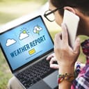 Man looking at weather report on his laptop while talking on smartphone
