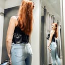 Young slim girl trying on new jeans in the fitting room in the store.