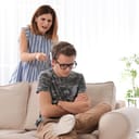 A sad boy sitting on a couch being criticized by a woman
