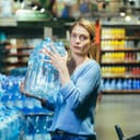 portrait of a frightened female shopper in a supermarket holding plastic water bottles