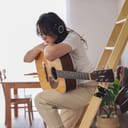 A sad young woman with headphones leaning over her guitar