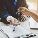 Person handing over their car keys to another person over a piece of paper reading 'contract'