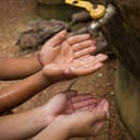 Kids' hands under a dripping outdoor faucet