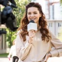A young smiling journalist talking into a microphone while looking at the camera