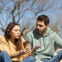 young couple arguing while sitting in the park, woman is holding a paper cup of coffee