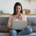 Smiling young woman using laptop, sitting on couch at home, beautiful girl shopping or chatting online in social network, having fun, watching movie, freelancer working on computer project