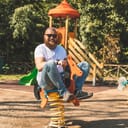 Playful man (dad) riding wooden rocking horse in a park - adult guy (hipster with beard) having fun on a playground
