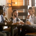 group of five friends laughing and enjoying coffee together in a café environment