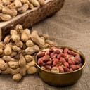 Peanuts in nutshell on a piece of wood and peeled peanuts in golden bowl on sackcloth