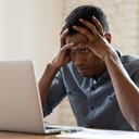 A man looking at a lap top in disbelief holding his head with his hands
