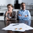 divorce papers and wedding rings in focus and an angry couple in the background