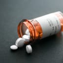An open bottle of pills lying sideways with some pills coming out of it