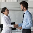 two business professionals happily shaking hands and smiling in an office