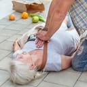 Close-up of a man administering CPR, to an elderly woman who has collapsed on the street.