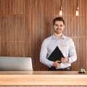 a receptionist holding a clipboard and  standing at a desk in a hotel lobby