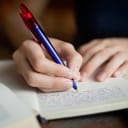 A closeup of a person writing in a notebook with a pen