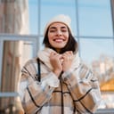 stylish attractive young smiling woman walking in street in winter outfit with coffee wearing checkered coat, white knitted hat and scarf, happy mood, fashion style trend
