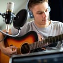 Young man wearing earphones playing the guitar in front of a studio microphone
