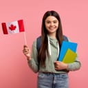 a portrait of a smiling young girl holding a Canadian flag in one hand and a couple of notebooks in the other