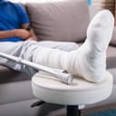 close-up of a man sitting in his living room with a cast on his broken leg and crutches next to it