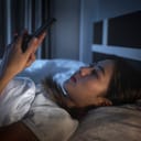 A young woman in bed using her phone