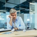 A sad gray-haired male architect sitting behind his desk in a contemporary office, reflecting on setbacks.