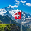 A Swiss flag on a pole with the Alps in the background