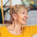 smiling mature woman wearing a yellow shirt and a hearing aid indoors