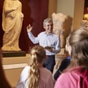 a teacher and pupils on a school field trip at a museum with a guide
