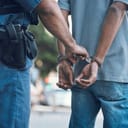 close-up of a police officer taking a handcuffed suspect into custody