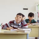A bored boy sitting in school with books and a notebook in front of him