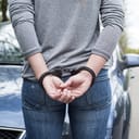 Handcuffed woman in front of a car