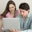 young couple appearing worried as they use a laptop to check something online